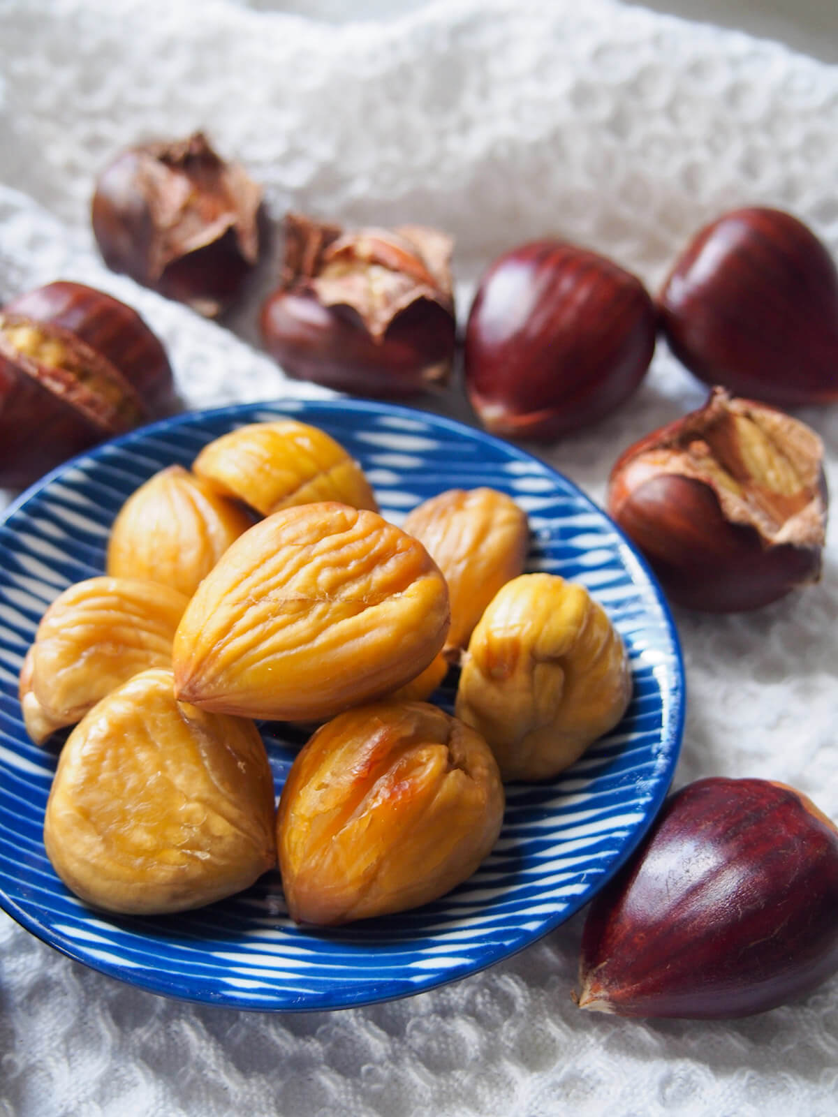 plate with roasted chestnuts slightly to side with more chestnuts to peel behind