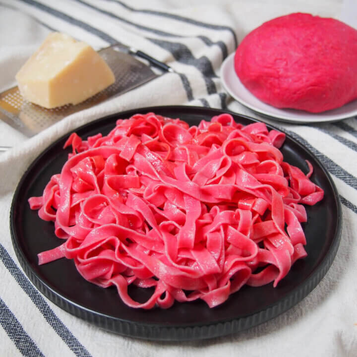 plate of beet pasta with cheese and ball of beet pasta dough behind.