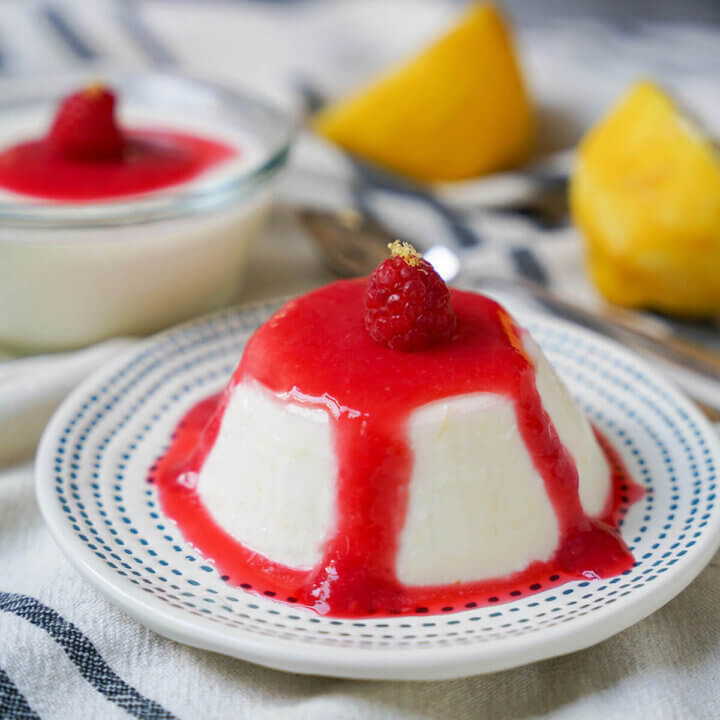 lemon panna cotta with raspberry coulis over top and lemon halves in background.