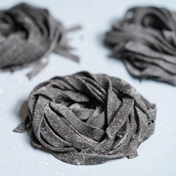 small stack of squid ink pasta on tray with others blurred behind.