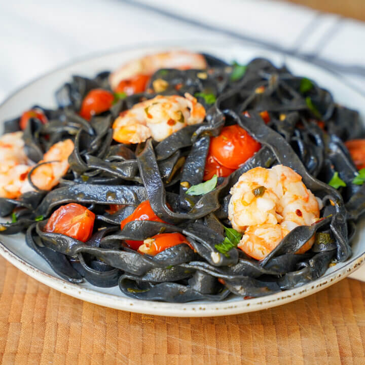 close view of plate of squid ink pasta with shrimp and tomato.