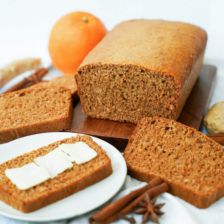 part loaf of pain d'epices, French spice bread, with slices to side and in front and one slice topped with butter.