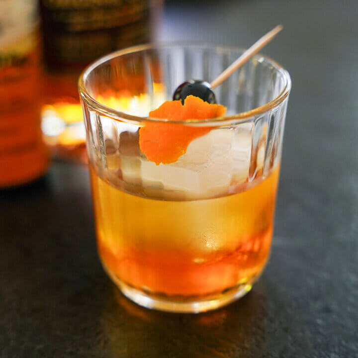 glass of rum old fashioned with cherry and orange peel garnish on top.