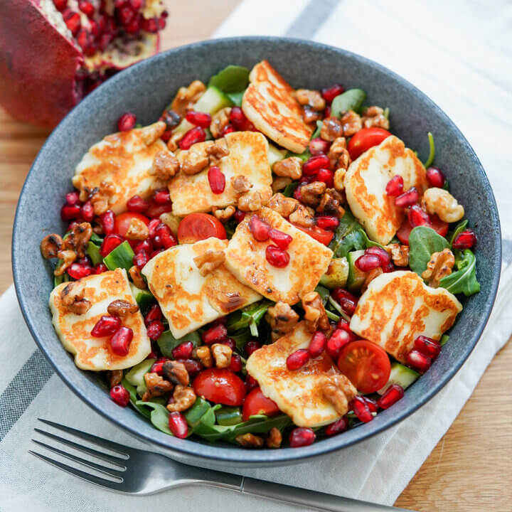 bowl of halloumi pomegranate salad with fork below bowl and cloth under.