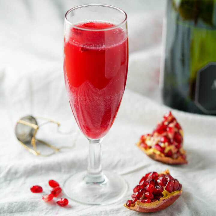 side view of glass of pomegranate mimosa with wedges of pomegranate to side and part botle in background.