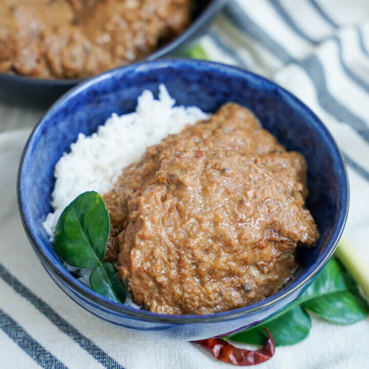 bowl of chicken rendang with lime leaf and chili under bowl.