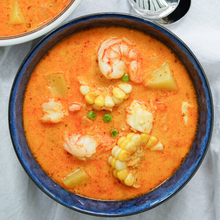 close up of chupe de camarones, Peruvian shrimp chowder showing shrimp and corn on top.